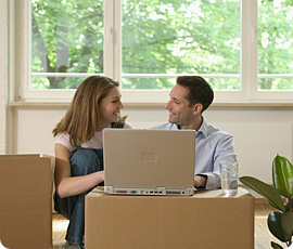 Smiling couple working on laptop among moving boxes.